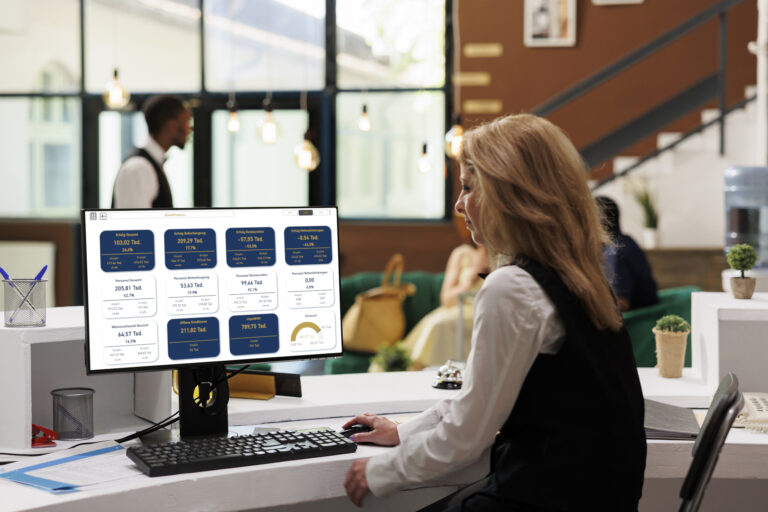 Receptionist working on desktop with blank copyspace chromakey display in luxury resort lounge area. Hotel lobby employee using computer with isolated whitescreen for registration at front desk.